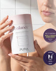Pura Collagen Balance supplement bottle with a clean label and a glass of water on a wooden surface, emphasizing health and wellness.